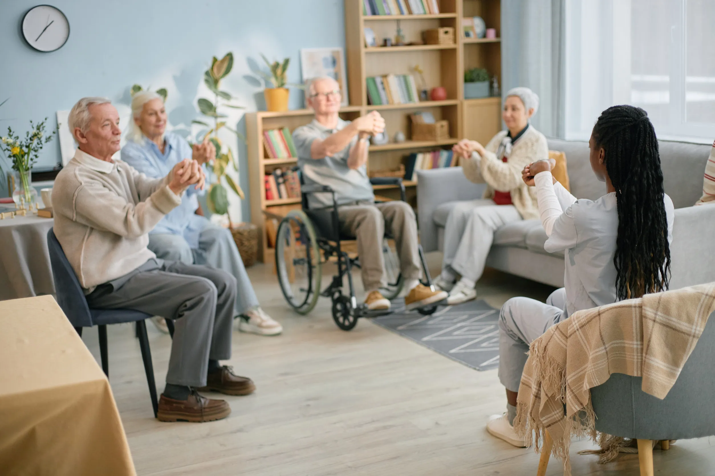 Elderly group engaging in chair exercise session in cozy room, guided by young instructor